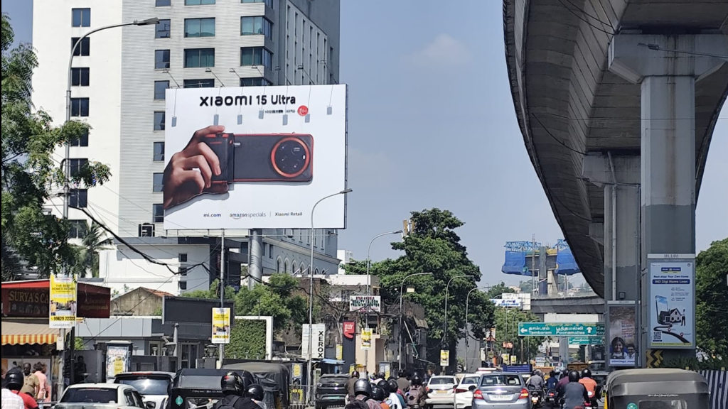 A massive billboard for the Xiaomi 15 Ultra overlooks a congested city intersection filled with commuters on motorcycles and cars beneath a clear sky.