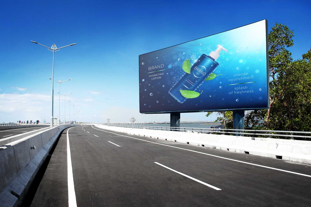 The image shows a wide, empty roadway—likely a highway or overpass—stretching into the distance under a clear blue sky. The road has clean lane markings and is bordered by low concrete barriers on both sides, with evenly spaced streetlights lining the left side.

On the right side of the road, there’s a large roadside billboard mounted on two supports. The billboard displays an advertisement for a blue bottle of hydrating lotion. The design includes water splashes, green leaves, and phrases like “hydrating lotion,” “intense nourishment,” and “splash of freshness,” suggesting a skincare or cosmetic product. Trees and some greenery appear behind and beside the billboard.

Overall, the scene feels bright, modern, and minimal, with no traffic or pedestrians visible.