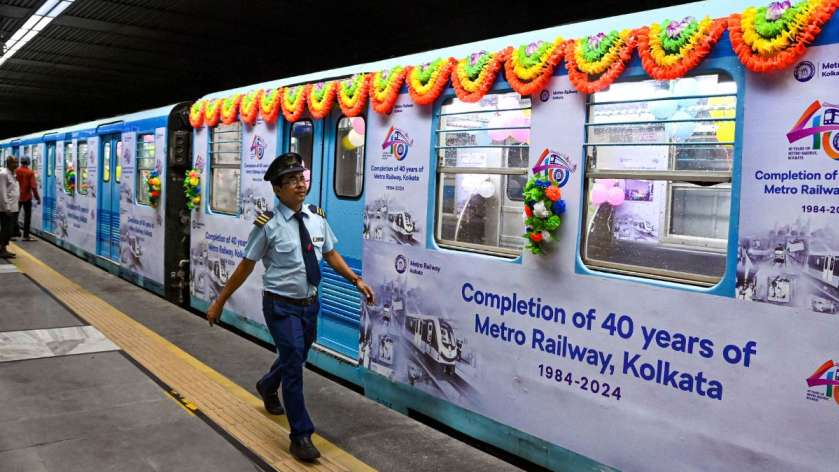 A blue metro train in Kolkata is fully wrapped in commemorative vinyl graphics celebrating 40 years of service, featuring marigold garlands and historical imagery as a transit official walks by.