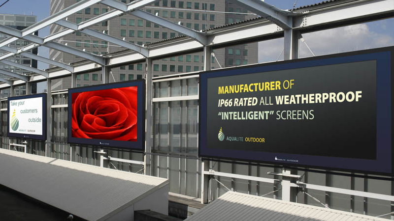Three large, weatherproof digital screens are mounted on an outdoor structural frame, with the primary display promoting Aqualite Outdoor’s "intelligent" IP66-rated screens for various commercial environments.