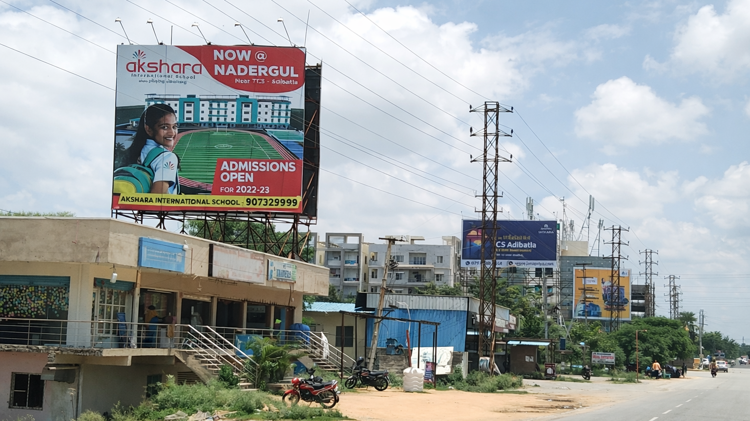 Large roadside billboard advertising Akshara International School admissions near Nadergul with campus image and student visual