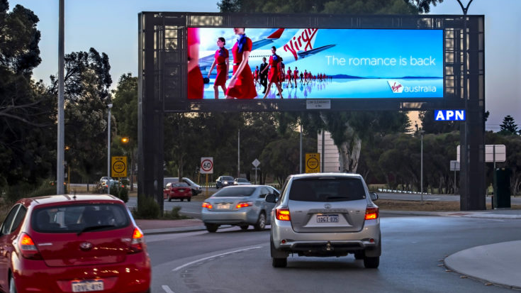Digital highway billboard advertising Virgin Australia airline with cars driving on road at dusk