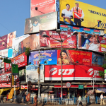 Multiple outdoor billboards and hoardings at a busy urban intersection in India showcasing diverse brand advertisements and high visibility outdoor media