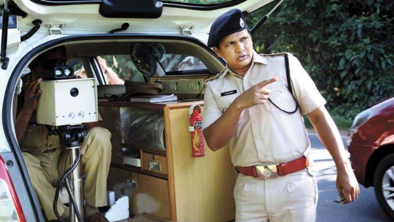 Indian police officer operating speed monitoring equipment from patrol vehicle during traffic enforcement
