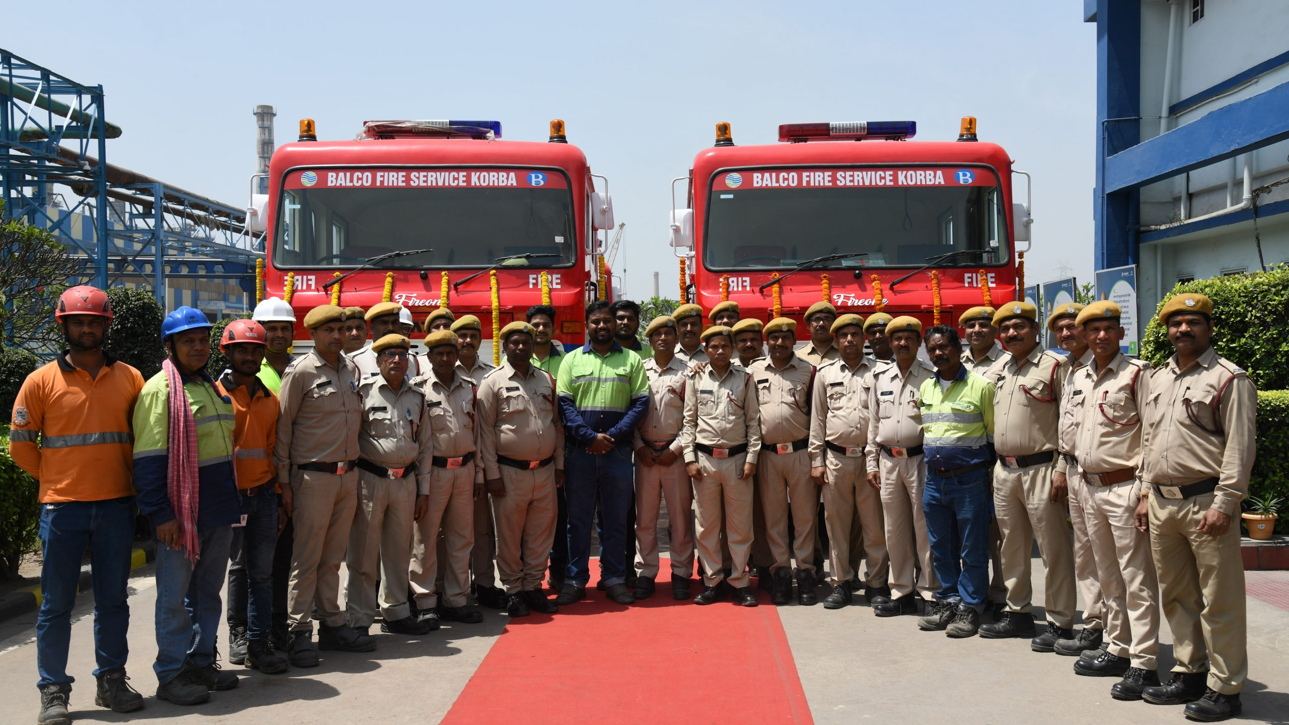 Fire service personnel standing in front of fire trucks during team gathering at industrial facility