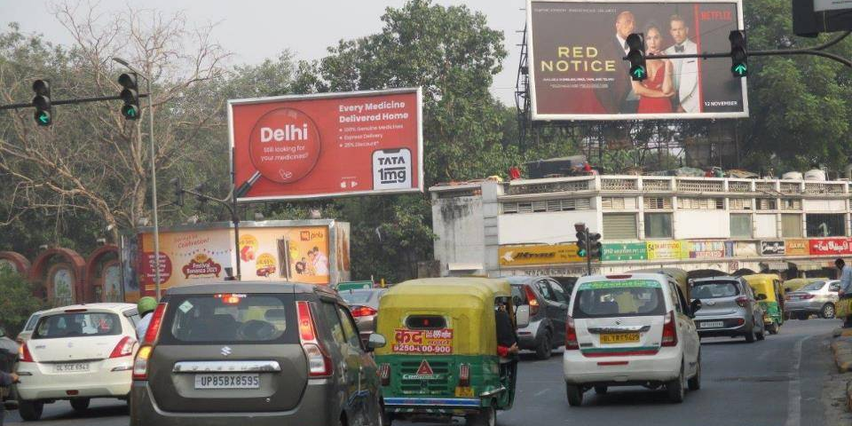 Busy urban road with multiple billboards including Tata 1mg healthcare ad and Netflix Red Notice movie promotion above traffic intersection