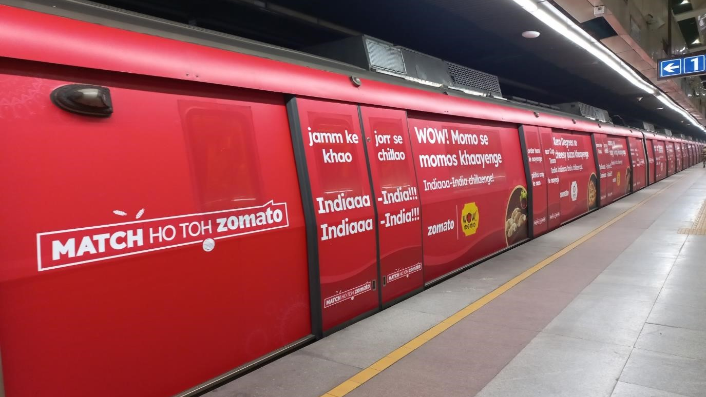 Zomato metro train wrap advertising campaign with bold red branding Full metro train branding by Zomato with red creative campaign promoting food delivery and momos messaging