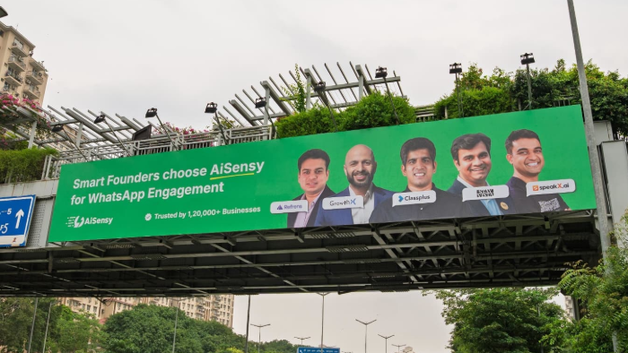 AiSensy outdoor bridge billboard campaign for WhatsApp marketing platform Large green bridge billboard advertising AiSensy WhatsApp engagement platform featuring founders and brand messaging
