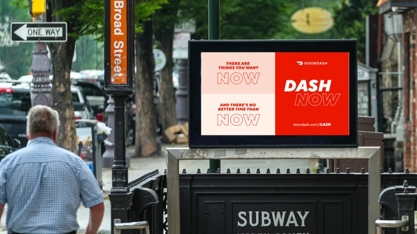 Street level digital out of home advertising screen near subway entrance displaying DoorDash campaign in urban environment