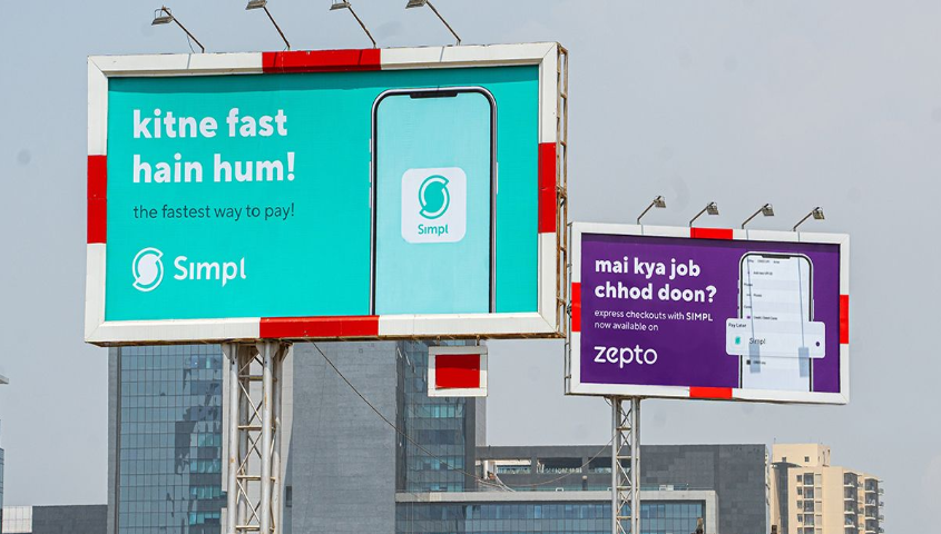 Two large outdoor billboards in an urban setting featuring a collaboration between Simpl and Zepto. The primary teal billboard asks, "kitne fast hain hum?" (How fast are we?), while the secondary purple billboard humorously references a popular meme with "mai kya job chhod doon?" (Should I leave my job?), promoting express checkouts for fast delivery services.