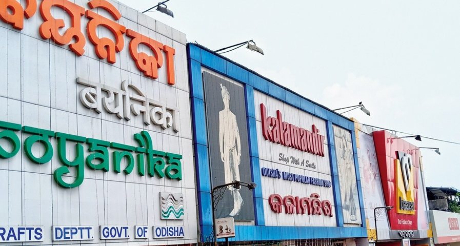 A streetside commercial building facade in Odisha featuring large multilingual storefront signage for Boyanika and Kalaniketan. The storefront displays bold branding in Odia and English with colorful exterior panels, fashion advertisements, and retail shop entrances along a busy urban road.