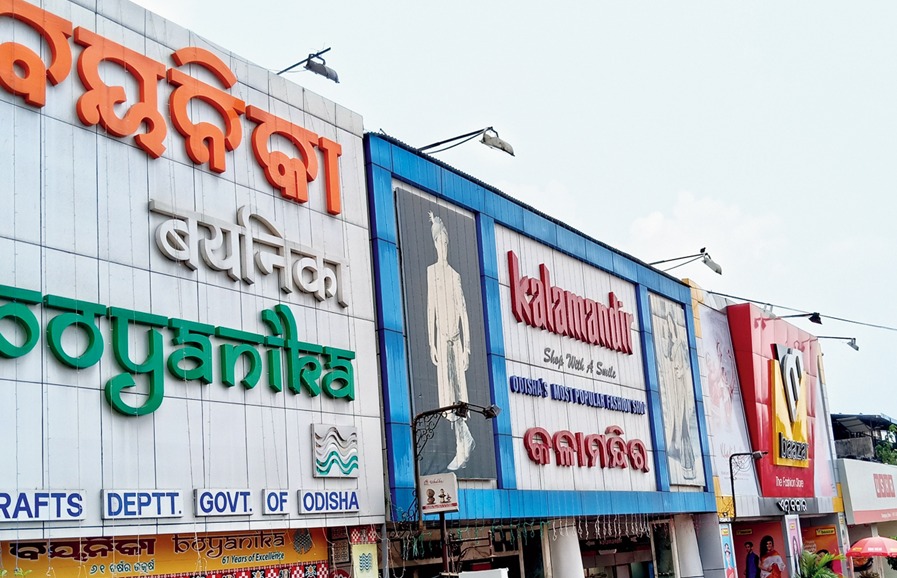 A streetside commercial building facade in Odisha featuring large multilingual storefront signage for Boyanika and Kalaniketan. The storefront displays bold branding in Odia and English with colorful exterior panels, fashion advertisements, and retail shop entrances along a busy urban road.