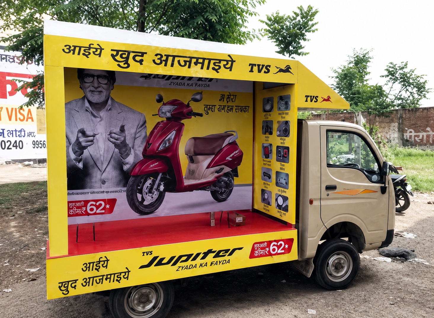 A TVS Jupiter mobile van activation featuring a bright yellow branded display vehicle parked outdoors with a large scooter visual, Hindi promotional messaging, and product feature panels. The campaign uses a regional language roadshow format to promote the scooter directly within local communities.