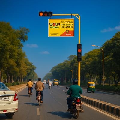 A traffic signal mounted advertising board displays a Wow! Momo promotion above a busy roadway. Positioned at an intersection where vehicles pause at red lights, the signal pole advertising format captures commuter attention and delivers targeted urban brand visibility.