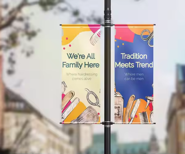 A pair of colorful street pole banners are mounted on a lamp post, displaying promotional messages for a hair salon. The lamp post advertising format uses eye level placement and repeated street visibility to engage pedestrians and commuters in busy urban areas.