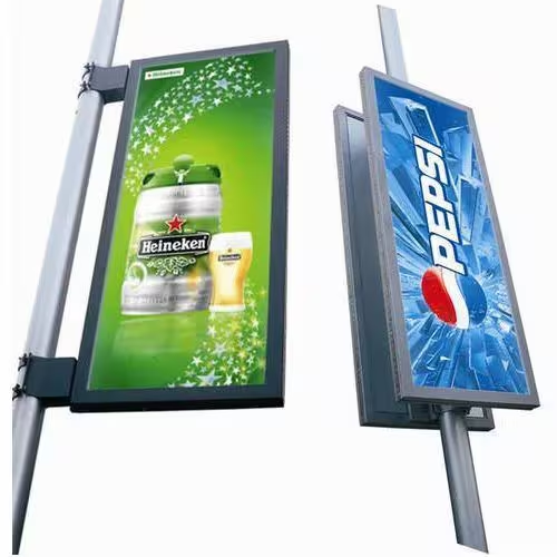 Double sided street pole advertising panels display Heineken and Pepsi campaigns on a roadside installation. Mounted at eye level along urban streets, the illuminated advertising format delivers continuous brand visibility to both pedestrians and passing traffic throughout the day and night.