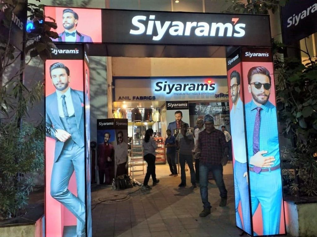 A large illuminated Siyaram’s entrance arch surrounds the storefront, featuring full height fashion visuals and branded display panels. The experiential retail branding installation transforms the store entrance into a high impact customer touchpoint, enhancing visibility and attracting shoppers from a distance.