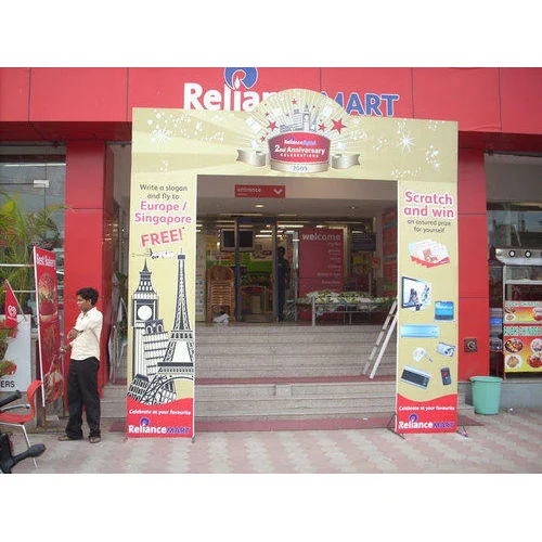 A promotional arch gate installed at the entrance of a Reliance Mart store to celebrate its anniversary campaign. The branded entry structure features festive graphics, prize promotion messaging, travel giveaway visuals, and scratch-and-win offers on both side pillars. Positioned directly at the store entrance, the arch gate transforms the retail frontage into a high-visibility promotional touchpoint that attracts shoppers and drives campaign engagement.