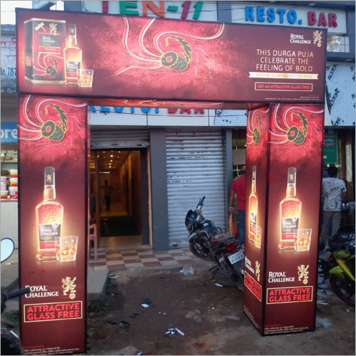 A branded Royal Challenge promotional arch gate installed at the entrance of a restaurant, featuring illuminated product visuals, festive themed graphics, and campaign messaging on both side pillars and the overhead panel. The high visibility entry branding transforms the storefront into an immersive brand experience and attracts attention from pedestrians and visitors.
