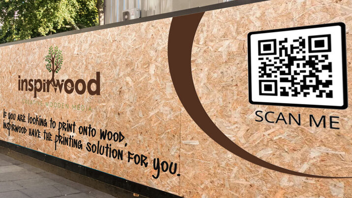 Tactile OOH with QR Integration: An outdoor hoarding for "Inspirwood" uses a textured wooden-print aesthetic to showcase their printing solutions, featuring a prominent "SCAN ME" QR code to drive mobile traffic.