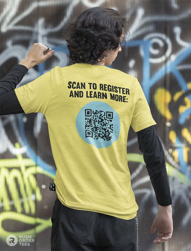 A custom branded t-shirt featuring a large QR code and the message “Scan to Register and Learn More” printed on the back. The image represents interactive t-shirt branding used for event promotions, registrations, awareness campaigns, and audience engagement through QR-enabled apparel marketing.