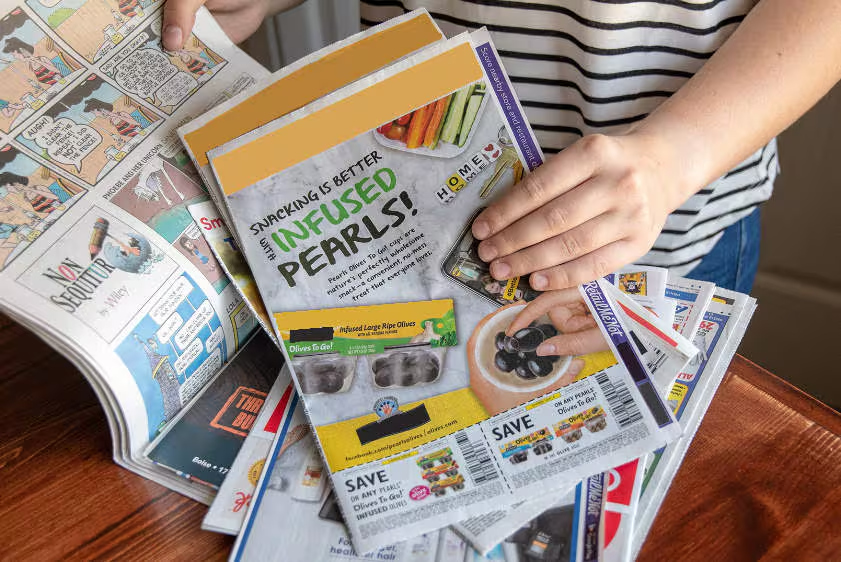 A newspaper insertion advertising campaign featuring a promotional product flyer placed inside a newspaper alongside discount coupons and printed advertisements. The image highlights newspaper insert marketing used to distribute brand promotions, product offers, and retail advertisements directly to readers through print newspaper circulation.