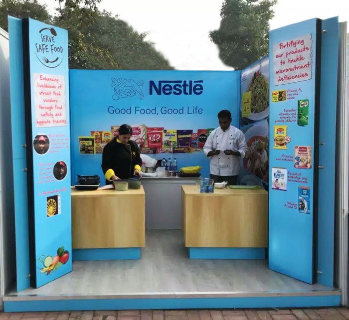 A Nestlé experiential society activation setup features a branded live cooking and food awareness booth with product displays, chefs, and interactive counters. The activation is designed to engage visitors through food demonstrations, nutrition awareness, and direct product interaction, creating an immersive on-ground brand experience focused on healthy living and consumer education.