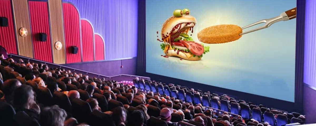 Cinema advertising displayed on a large movie theatre screen featuring a food brand promotion, capturing the attention of a seated audience in a packed cinema hall.