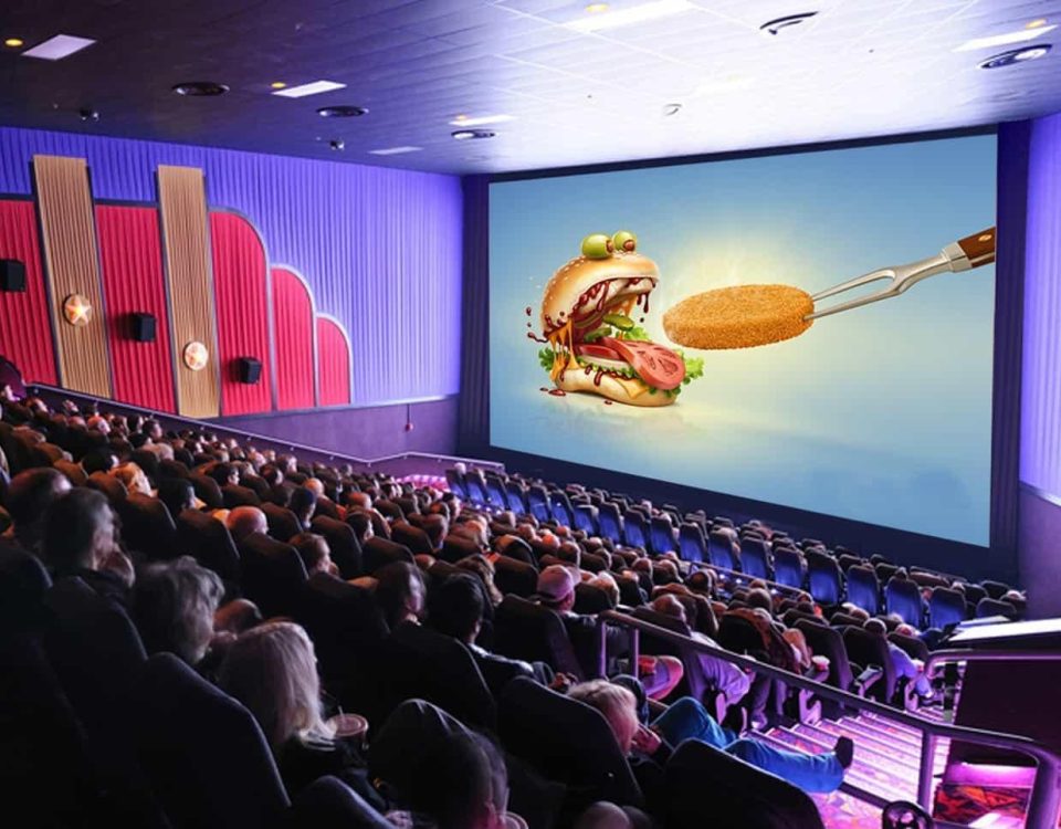 Cinema advertising displayed on a large movie theatre screen featuring a food brand promotion, capturing the attention of a seated audience in a packed cinema hall.