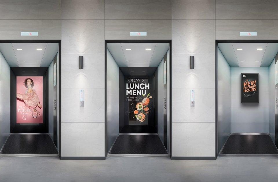 Elevator interior branding displaying full-height digital advertisements on the back walls of multiple elevators, showcasing fashion, restaurant, and promotional campaigns in a modern commercial building.